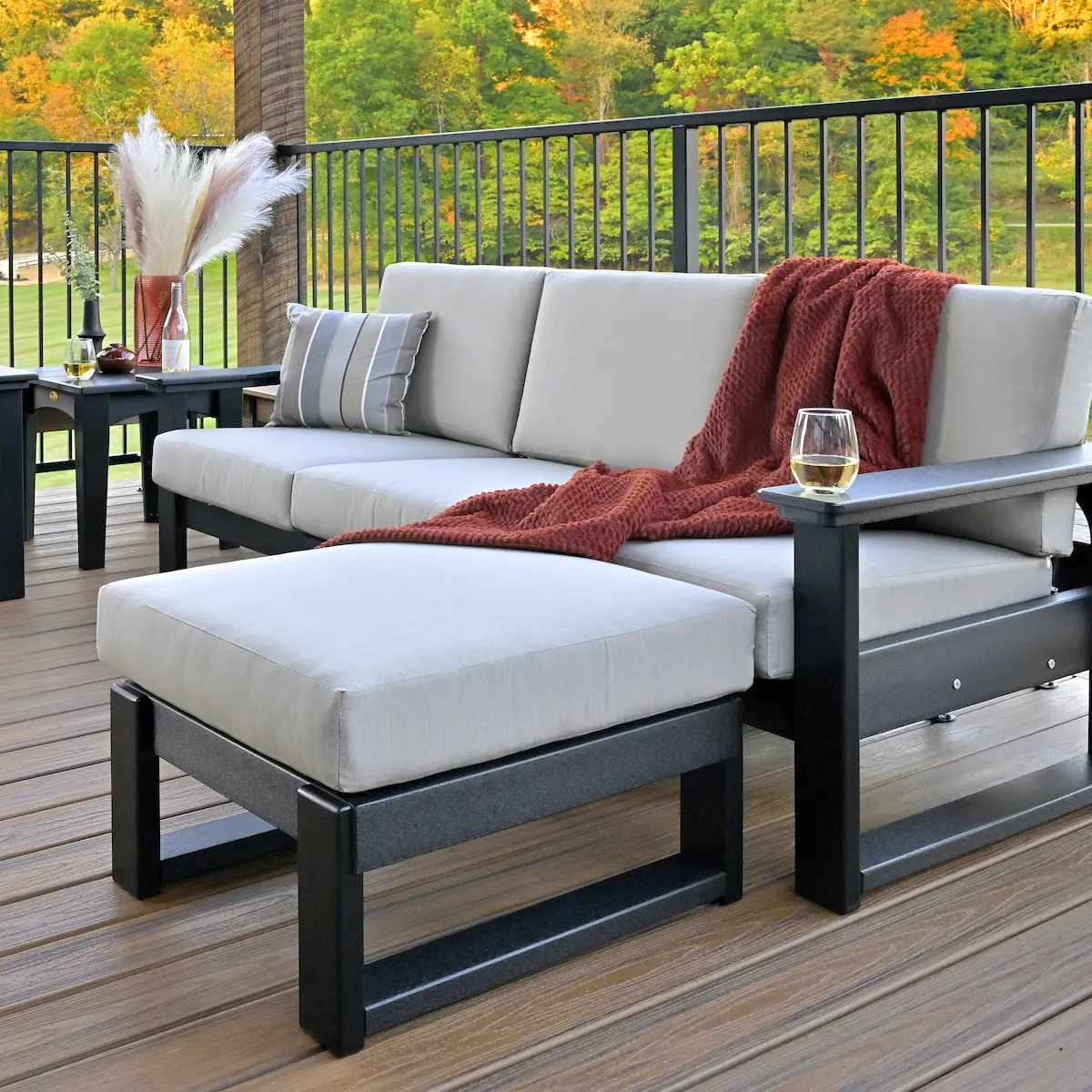 Modern Amish made outdoor patio seating with cushioned sectional sofa and ottoman on a composite deck, featuring American made craftsmanship and custom-built outdoor living design with black frame and neutral upholstery overlooking a scenic backyard.
